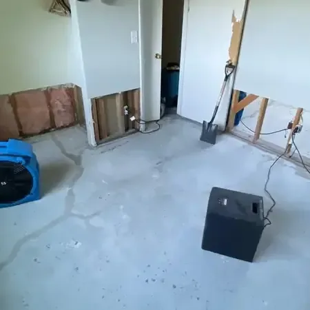 Manville water damage drying: air movers and a dehumidifier beside a bare floor and opened lower wall