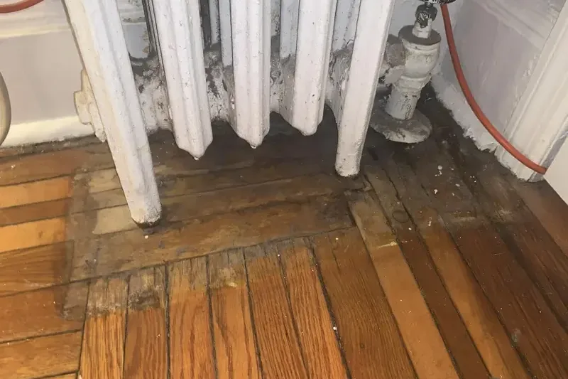 Water-stained oak floorboards beside a radiator valve in an apartment