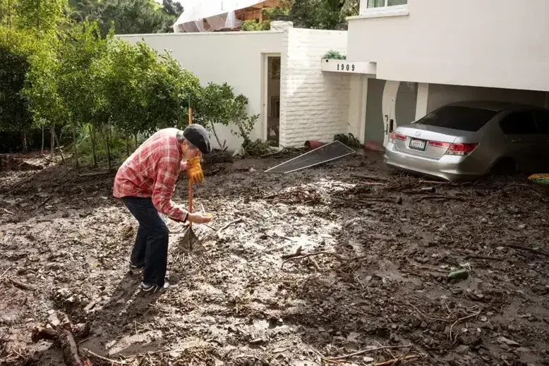 Homeowner clearing storm mud washed down against a house and garage